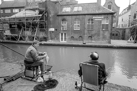 830234 Afbeelding van twee vissende mannen op de werf aan de Oudegracht te Utrecht, tegenover de Dansstudio De Boog, ...
